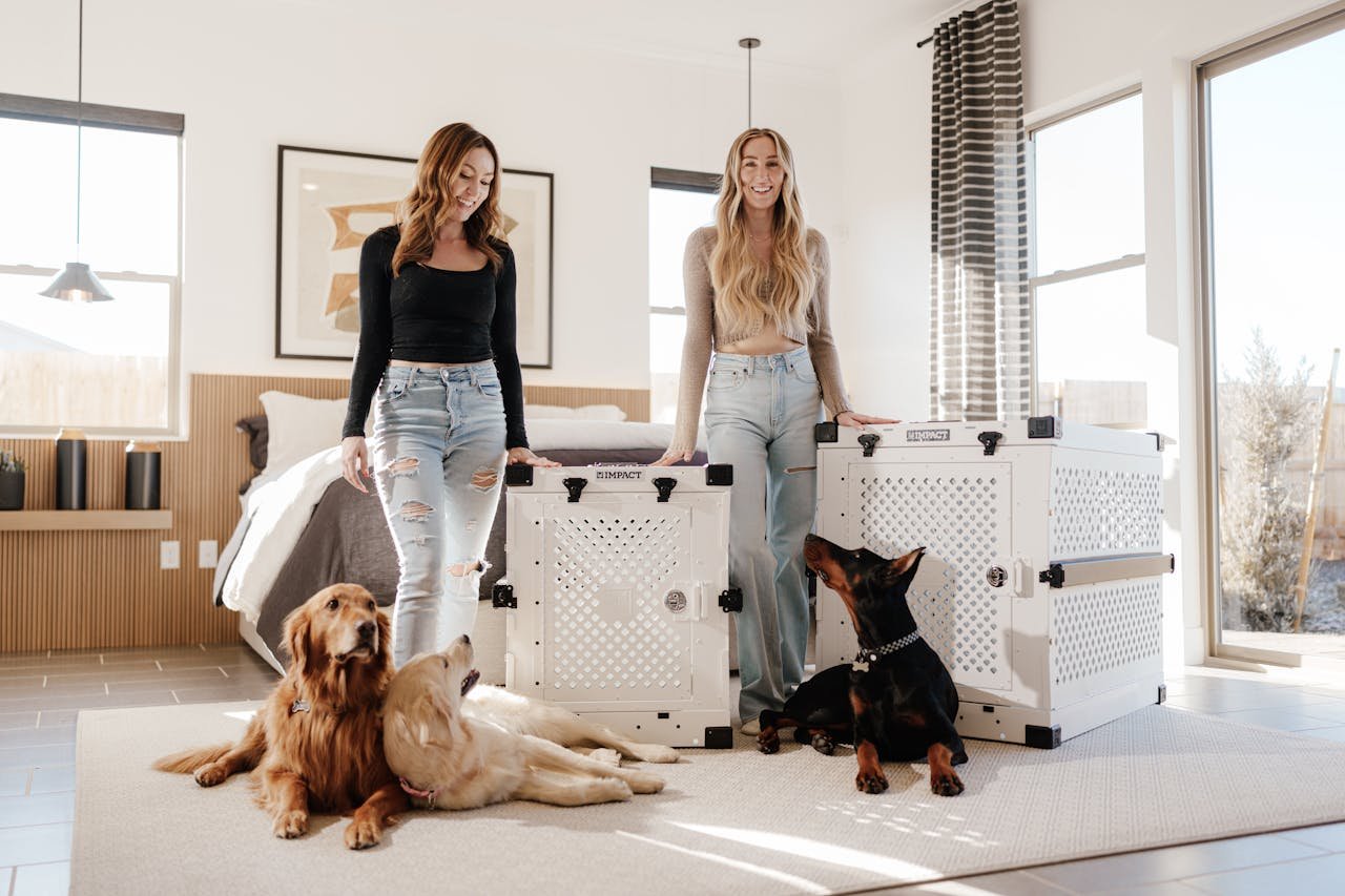 Two women with dogs showcasing premium, stylish dog crates in a well-lit modern bedroom.